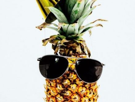 Photo of pineapple wearing black aviator style sunglasses and party hat